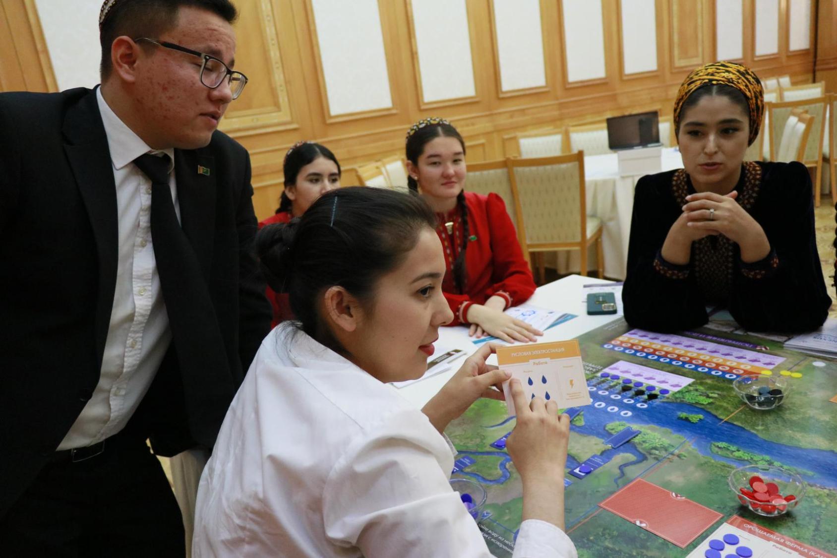 Участники сидят за столом и одна из девушек держит в руках игровую карточку в рамках тренинга.