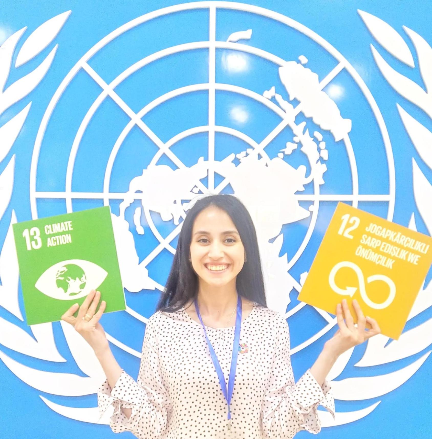 Девушка держит в руках карты ЦУР на фоне эмблемы ООН.