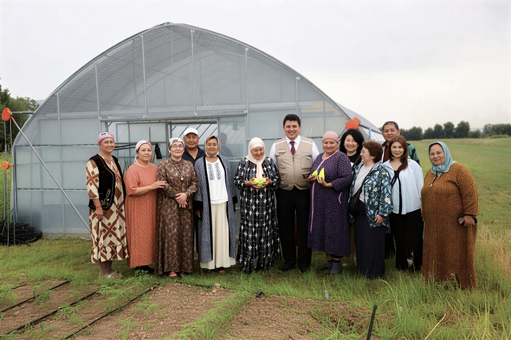 A group of women and a man pose for a photo in front of a hydroponics greenhouse in Kyrgyzstan.