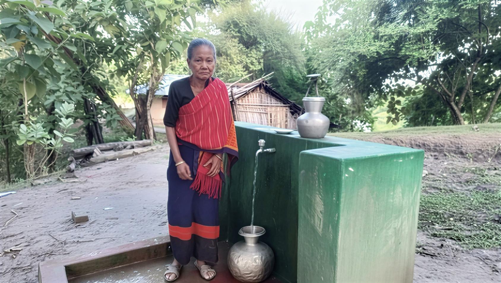 A woman in Bangladesh stands in front of a borehole.