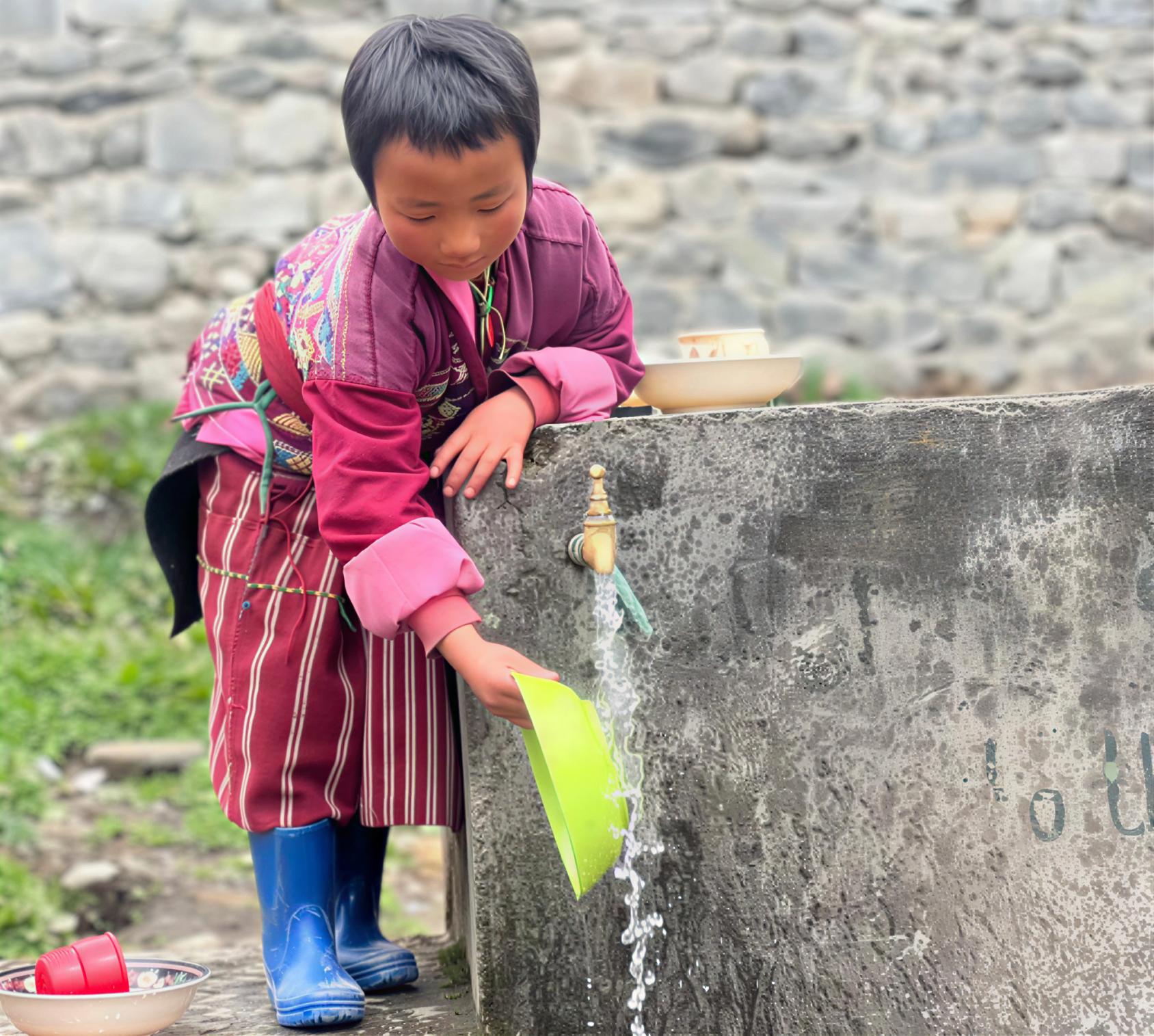 A child in Bhutan washes her plate at an outdoor water tap.