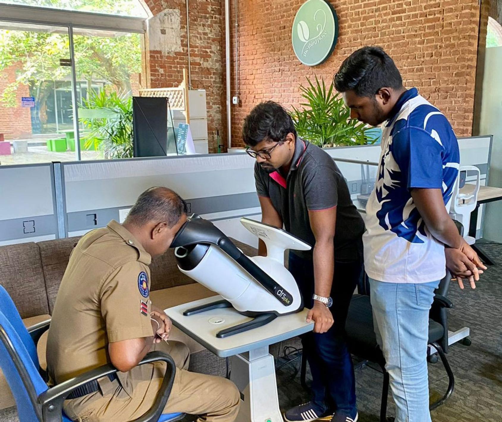 Two men in Sri Lanka watch another man test his eyes.