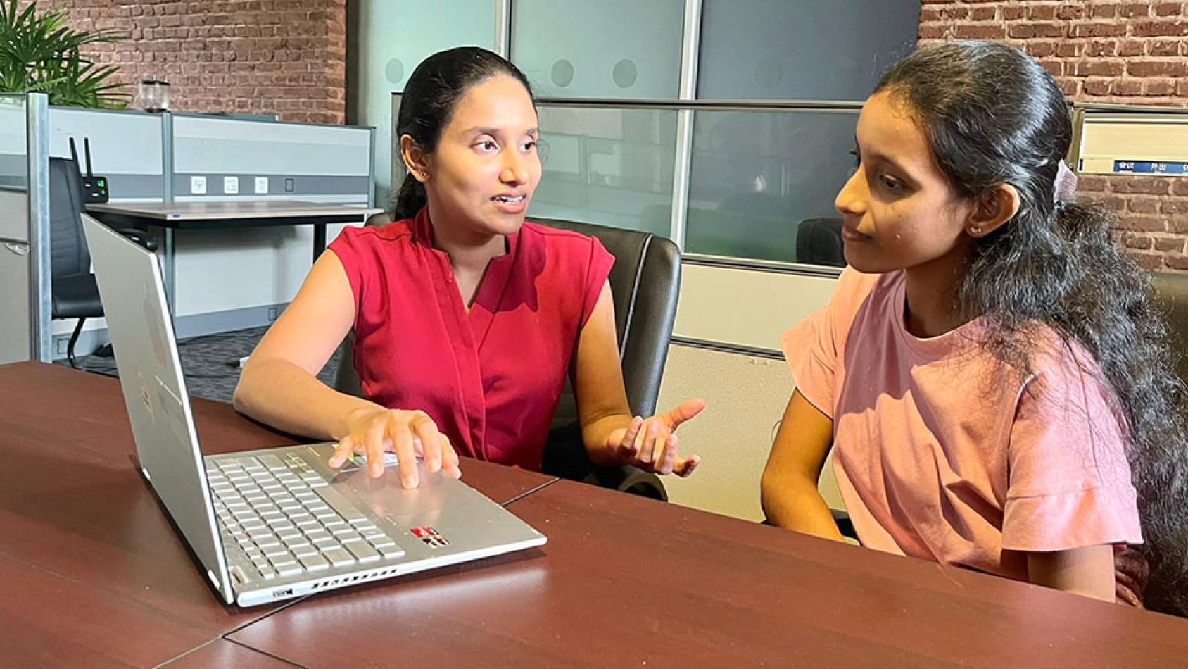 A woman in Sri Lanka demonstrates something on her laptop to a young girl.