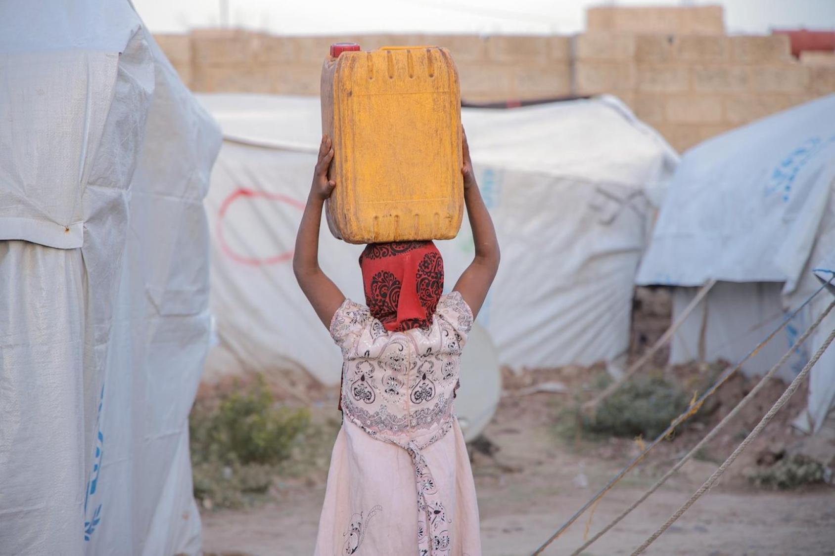  صورة لفتاة تحمل الماء عائدة إلى خيمتها في مخيم النازحين.