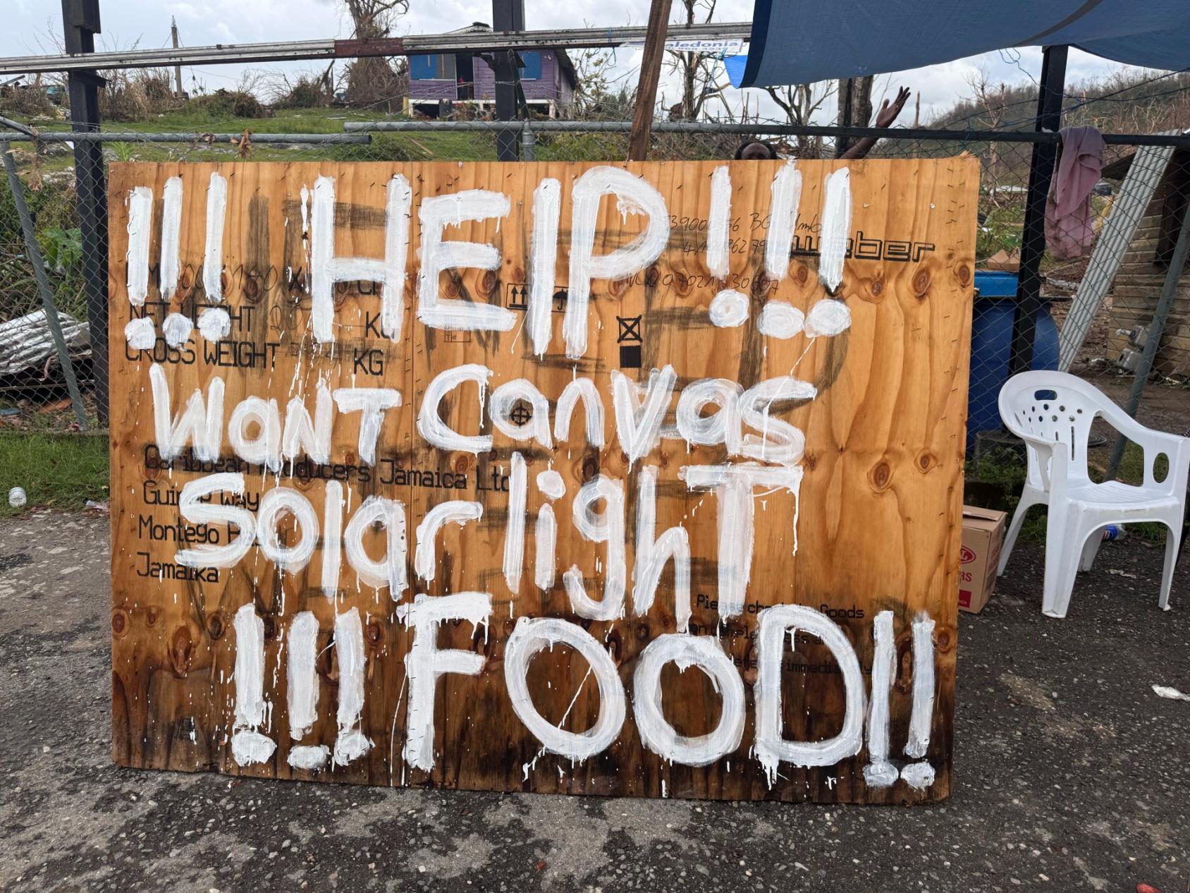 Une pancarte en bois faite par les habitants a été installée sur le bord de la route, appelant à une aide urgente alors que la communauté lutte pour reconstruire.