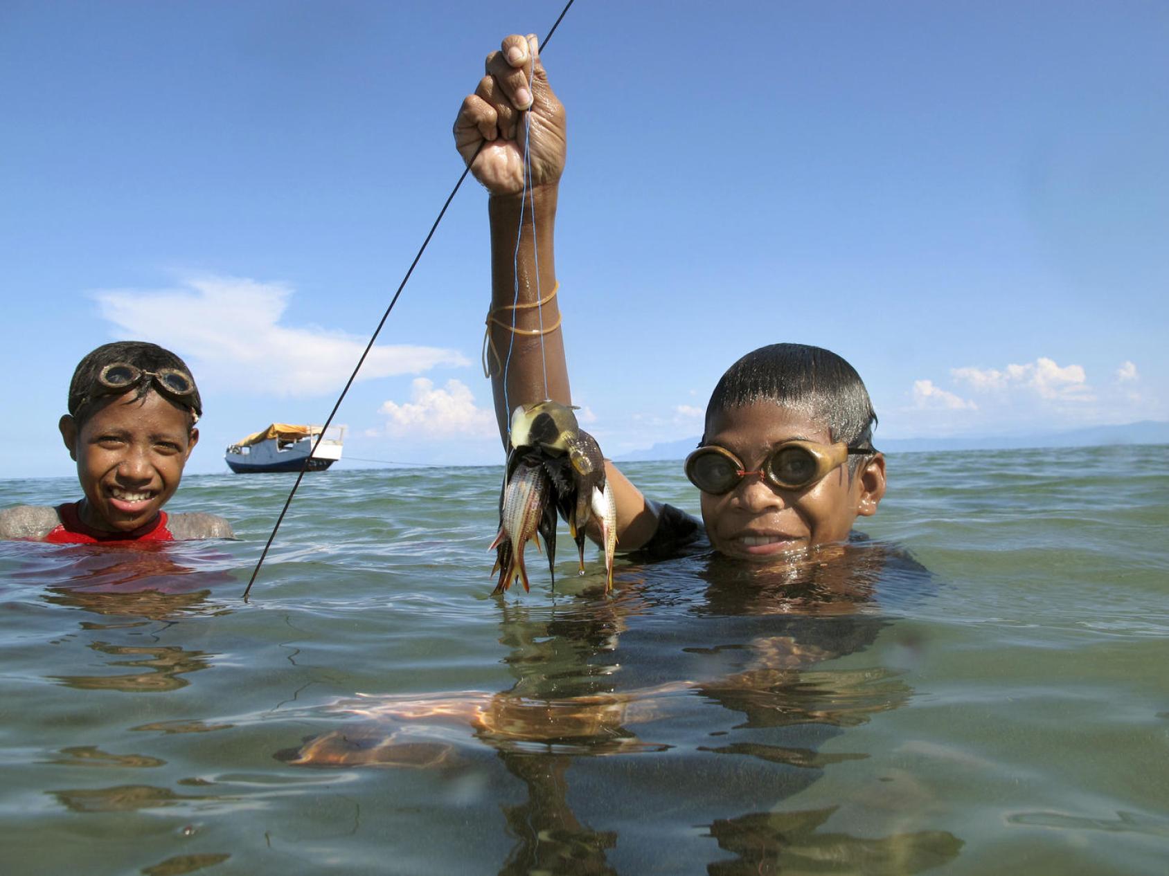 Two young boys in Timor-Leste show their catch in the ocean.
