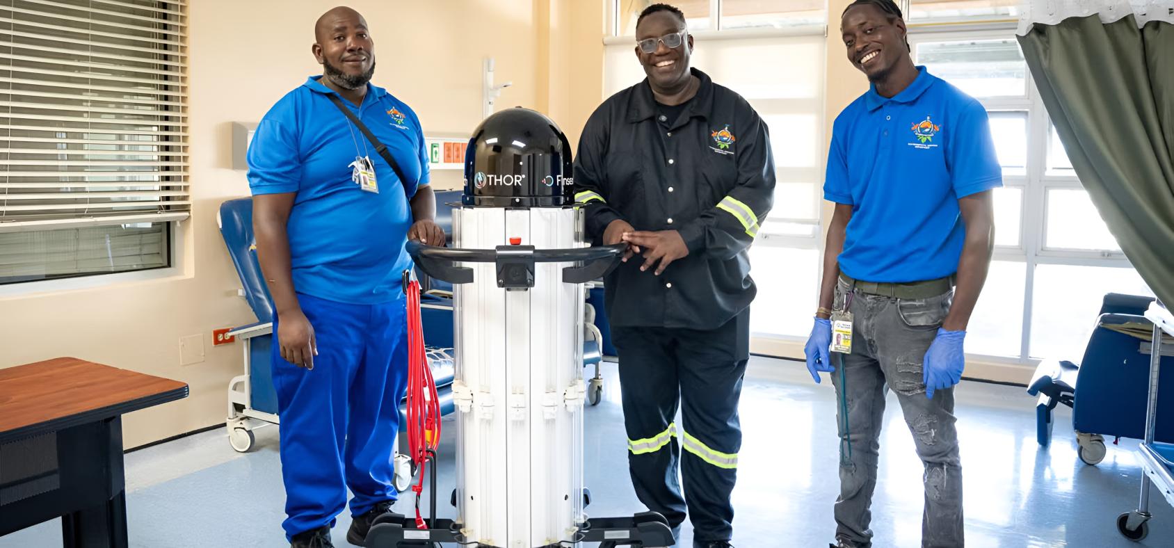 Three health workers in Trinidad and Tobago stand with a disinfecting robot.