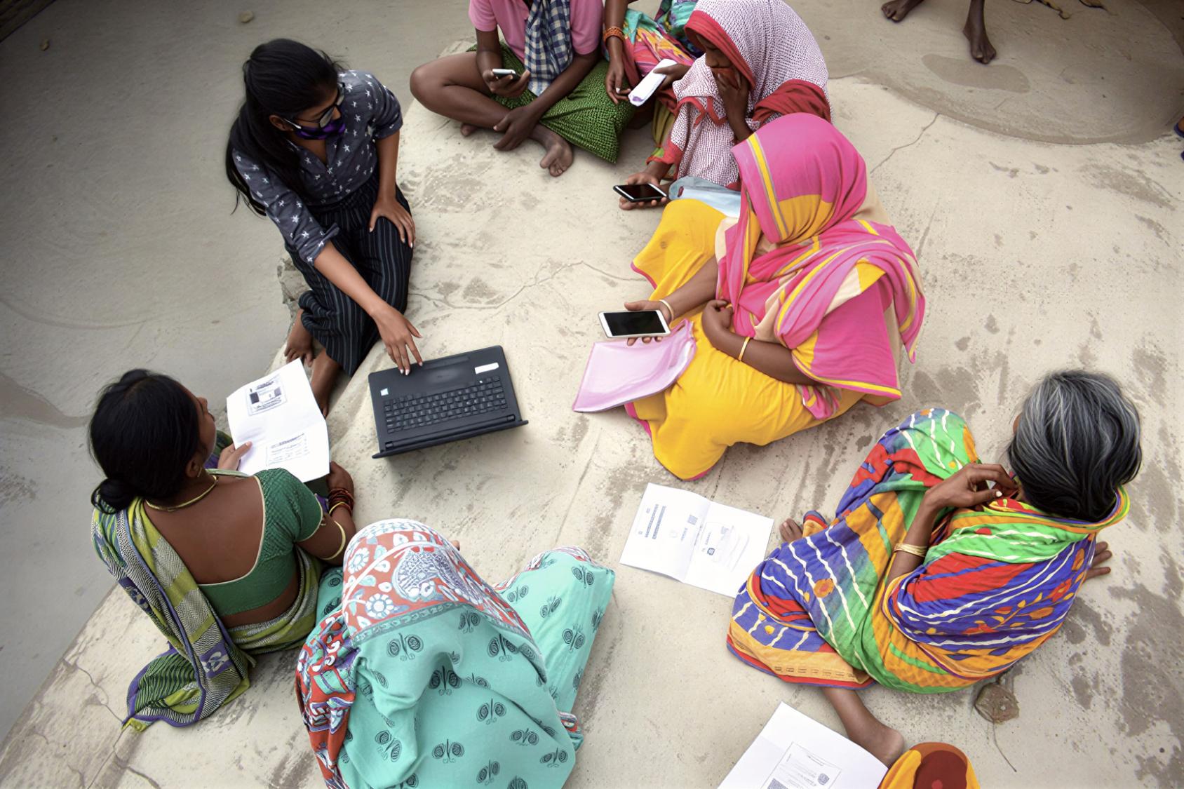 A group of women using their phones and a laptop. 