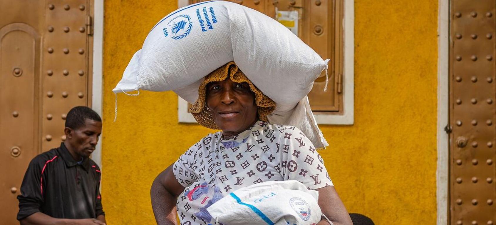 A woman in Haiti holds a bag of food while carrying another on her head.
