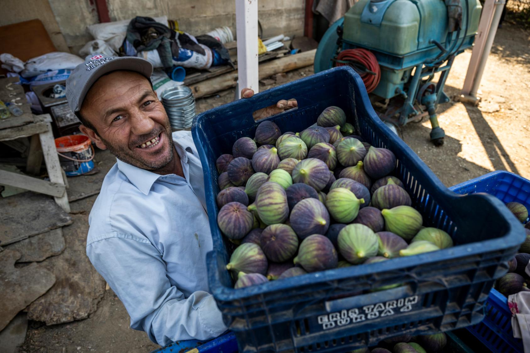 Улыбчивый мужчина держит ящик с инжиром.