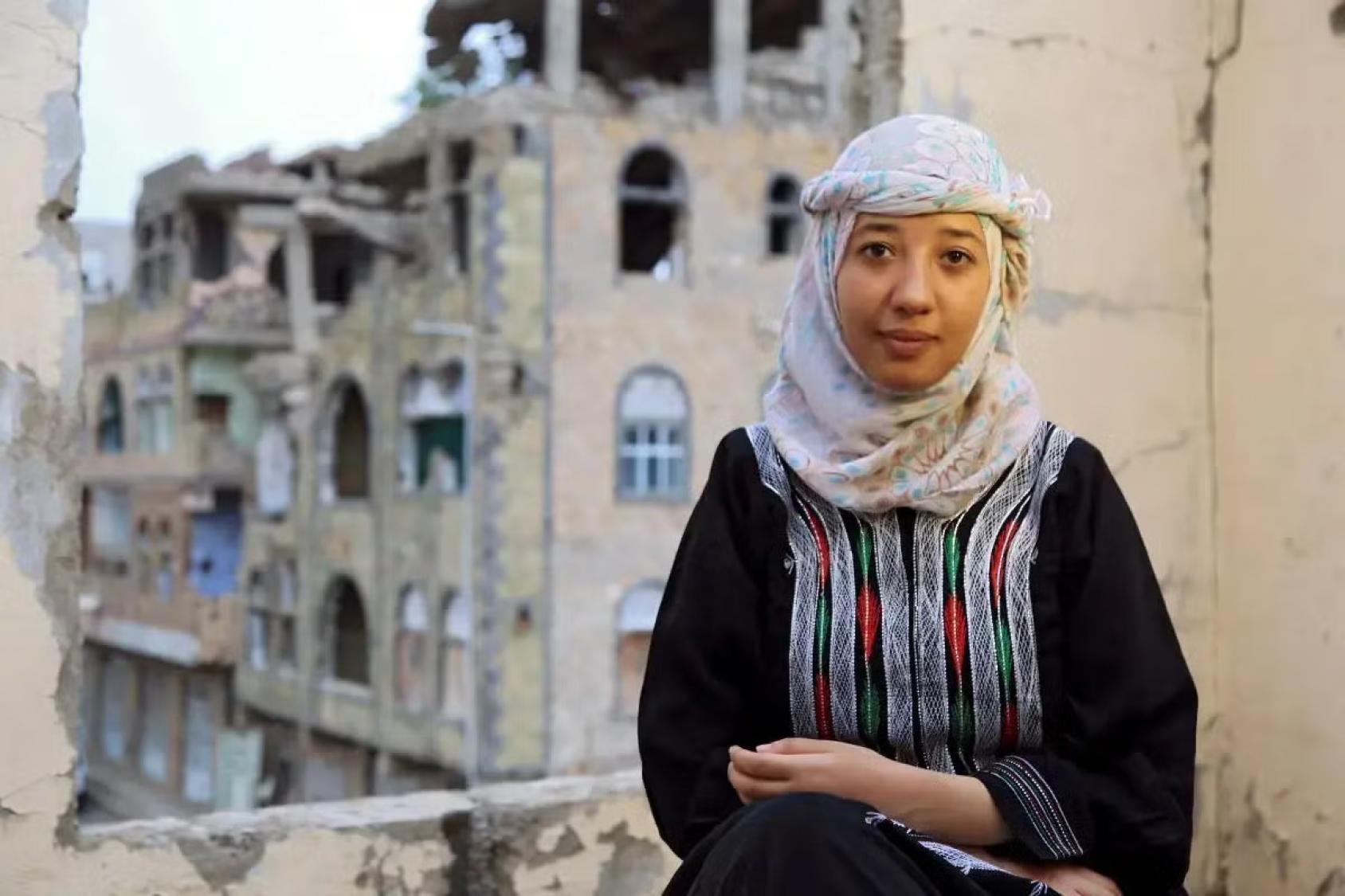 A young woman in front of a destroyed building.