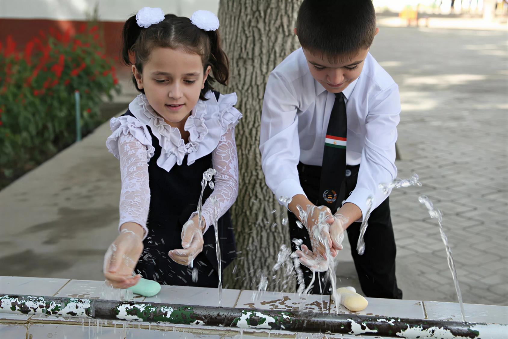 A boy and girl in Tajikistan wash their hands.