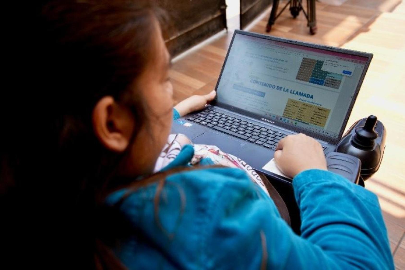 Una mujer, sentada en una silla de ruedas eléctrica, revisa un documento en su computadora.