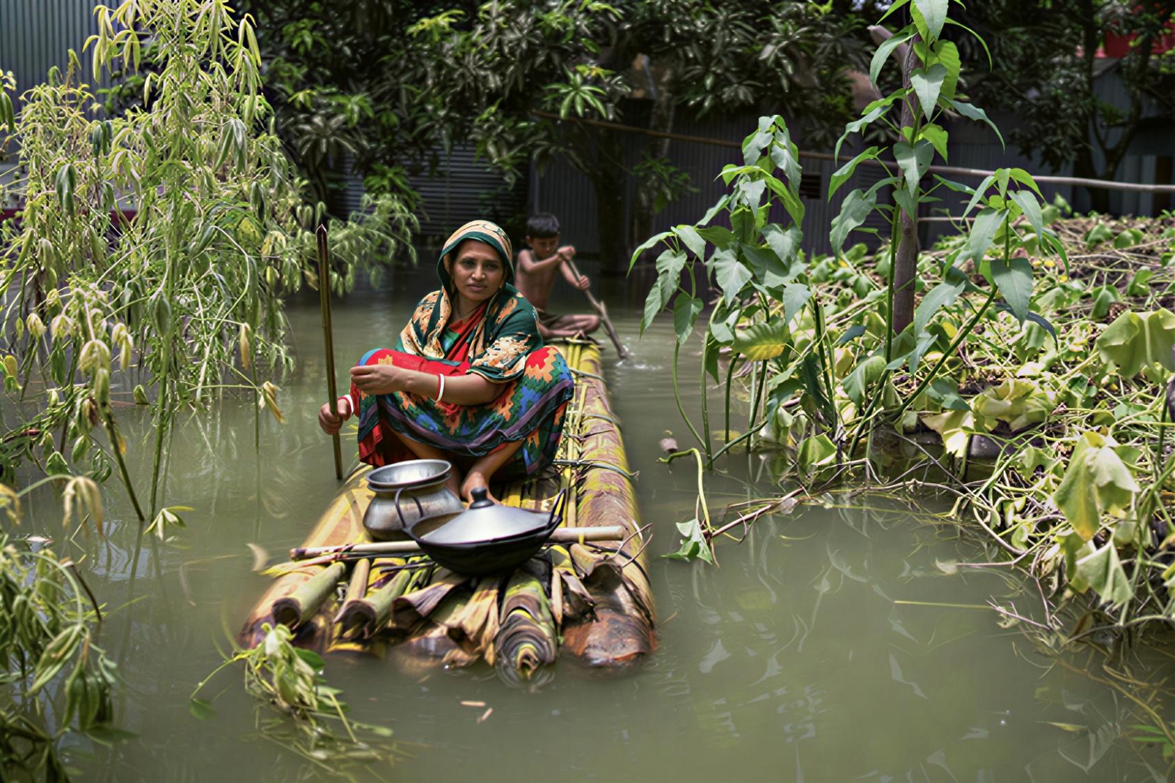A woman in Southeast Asia rows on a homemade canoe with her son behind her. 