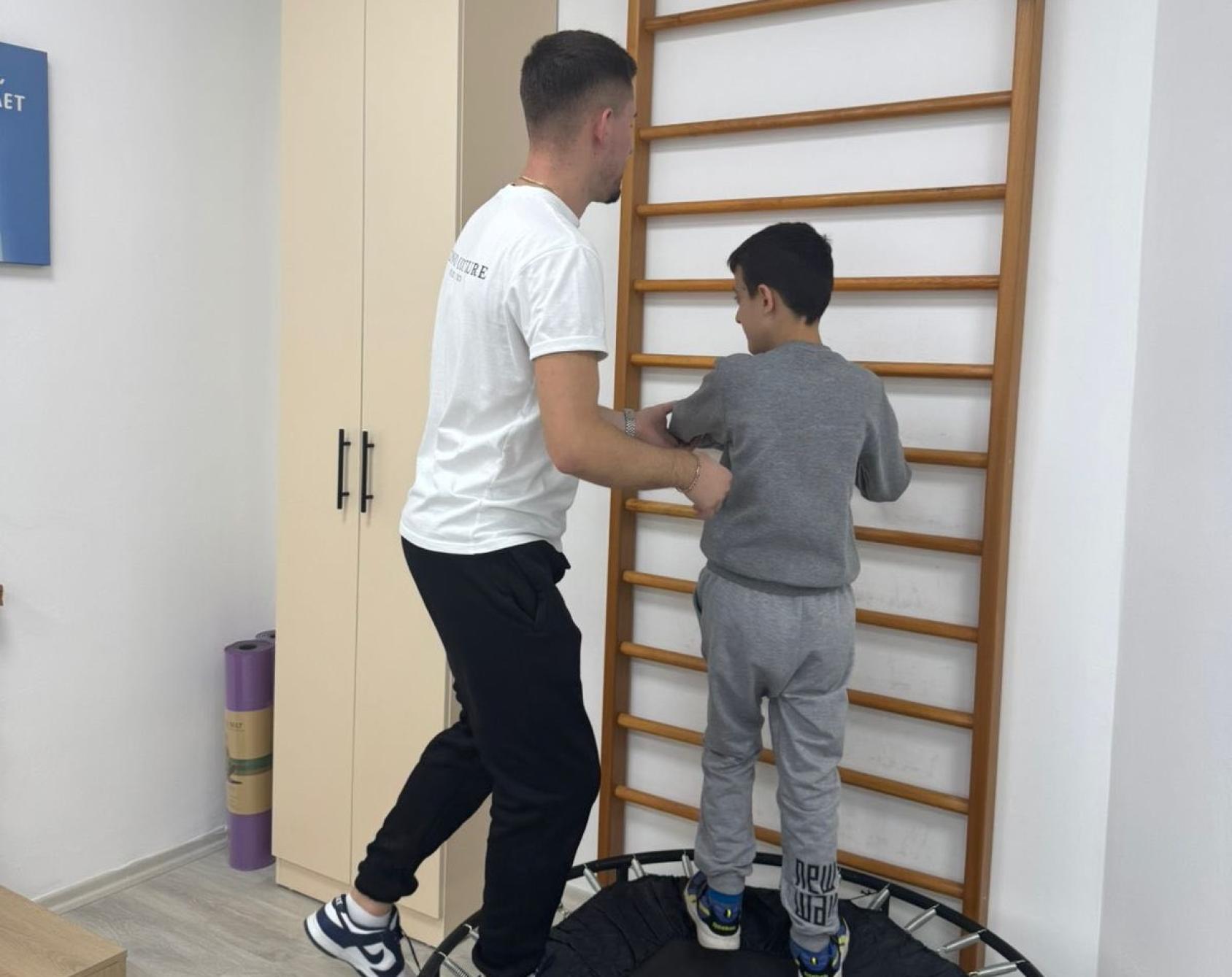 A young man plays on a small trampoline with a boy at a community centre in Albania.