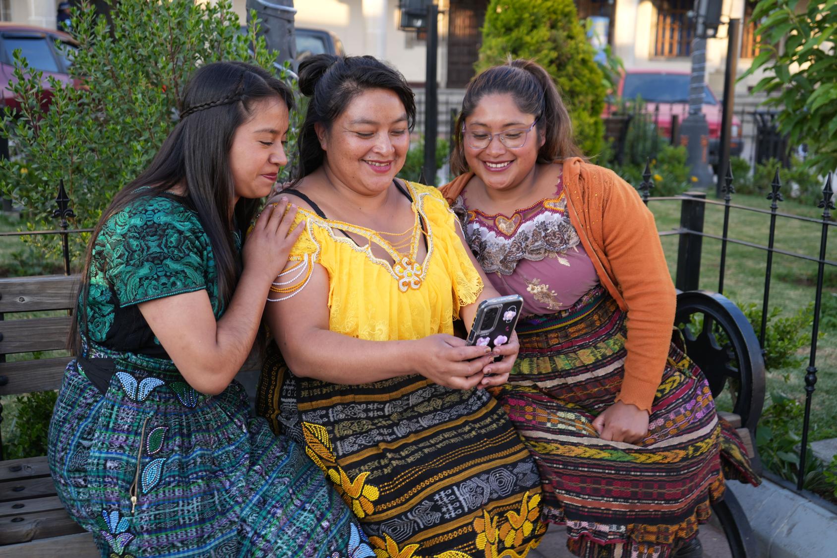 Three women in Guatemala look at something on a cell phone together.