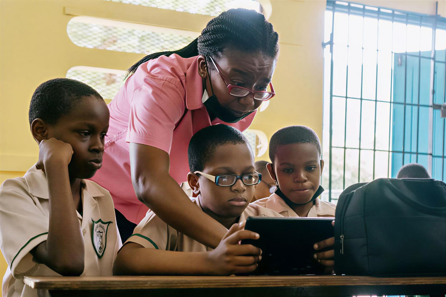 A teacher in Jamaica helps three students as they use a tablet.