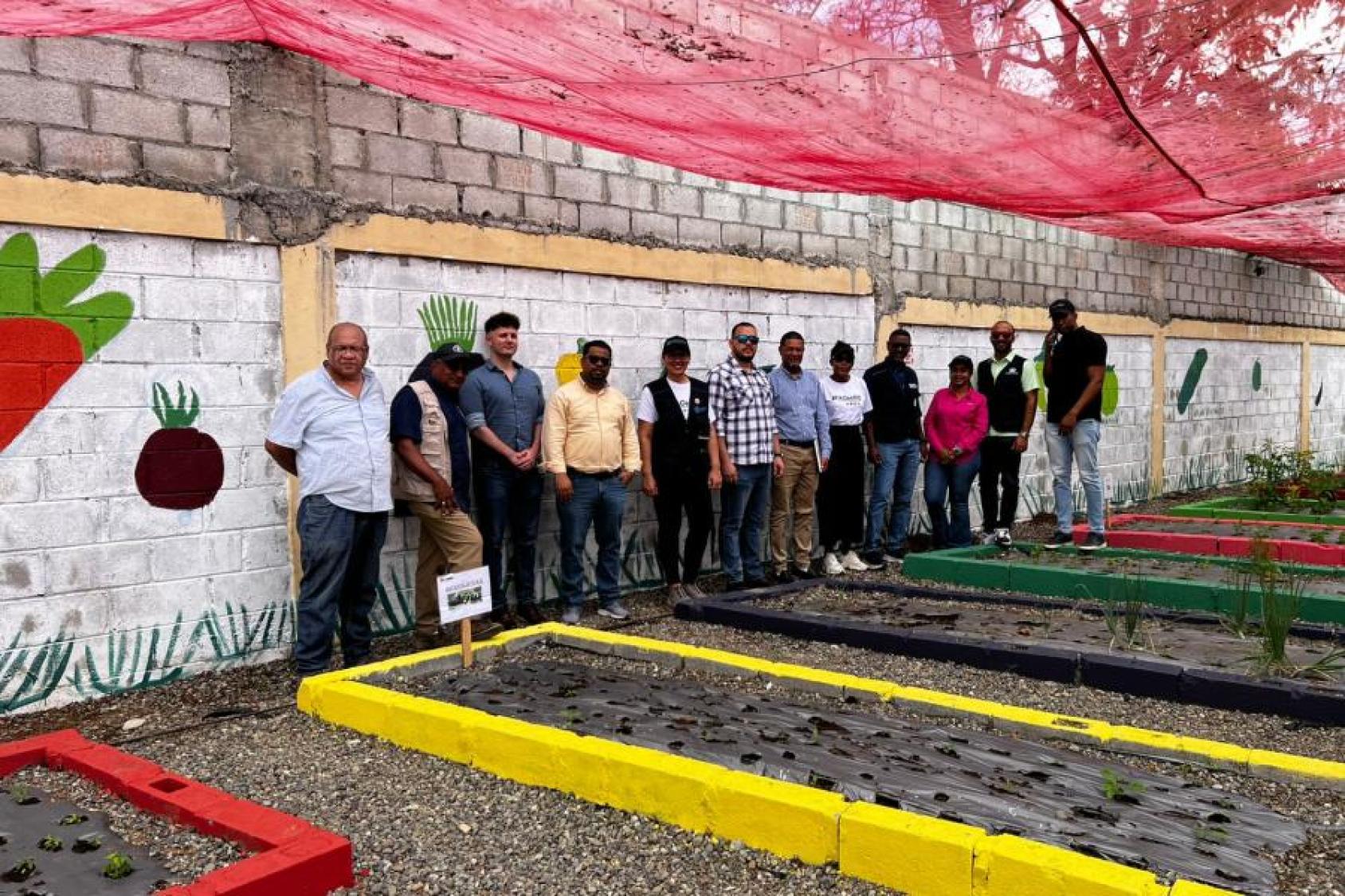 Un grupo de personas posa junto a bancales de cultivo en un huerto comunitario.