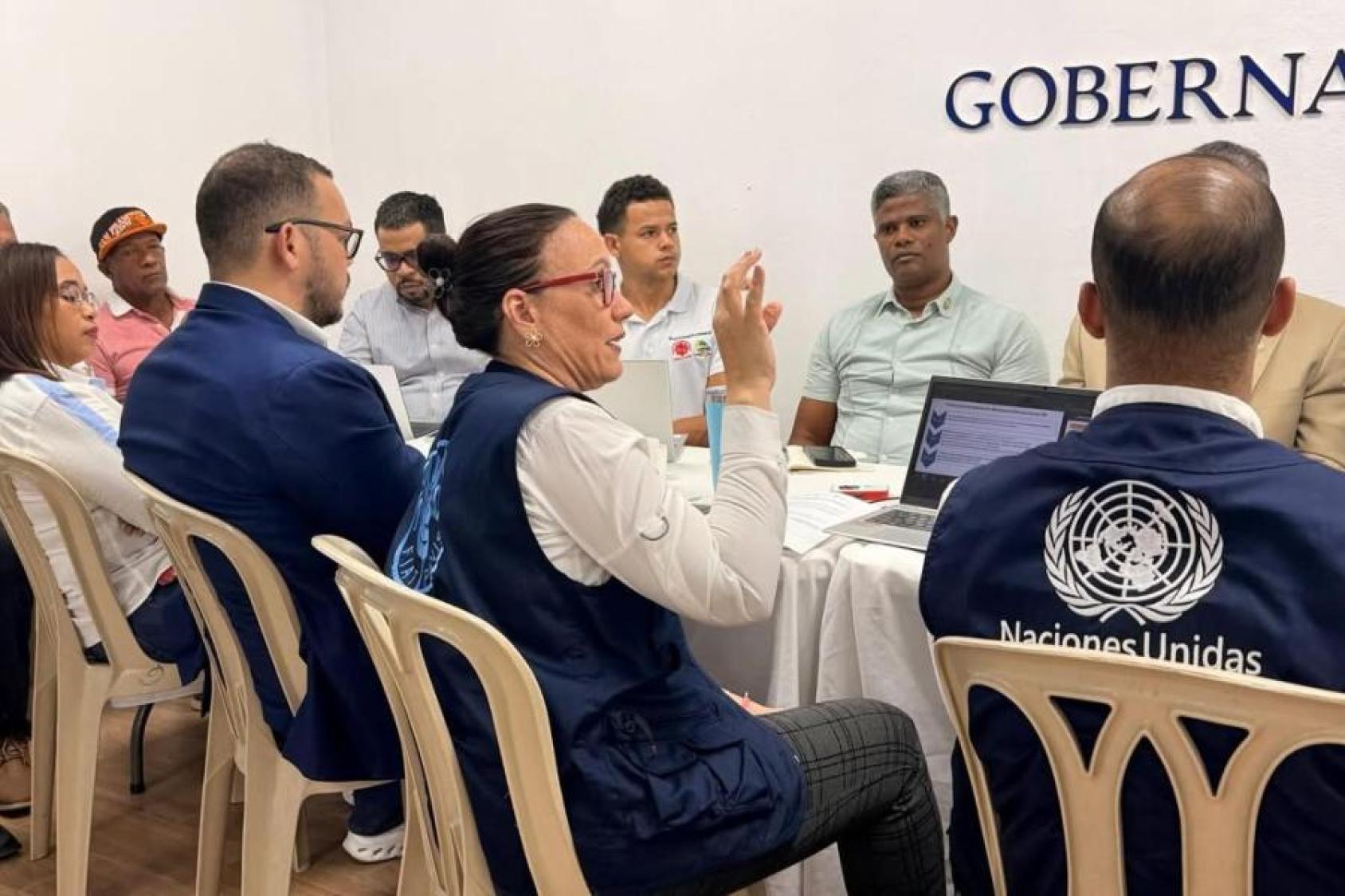 Participantes de una reunión institucional, incluidos representantes de Naciones Unidas, conversan alrededor de una mesa.