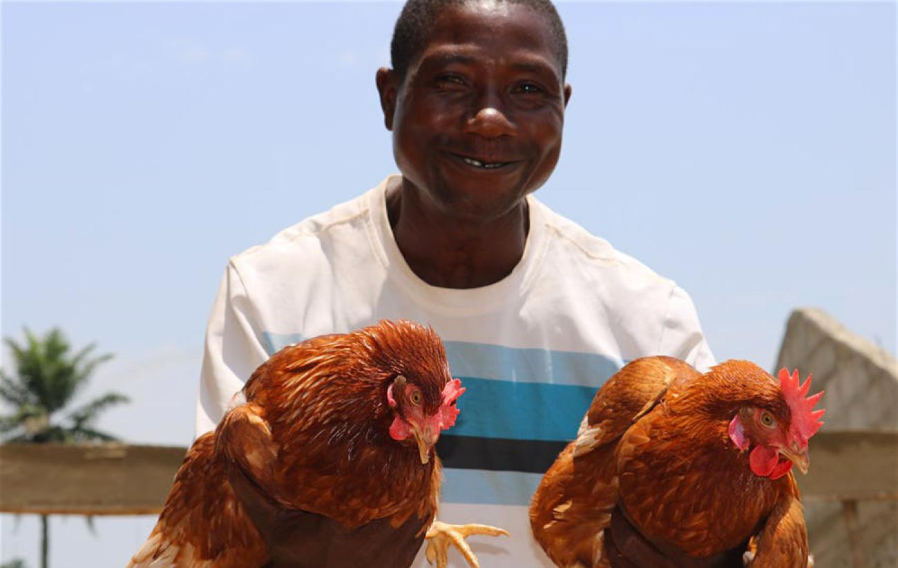 Tamby smiles at the camera as he holds to chickens. 
