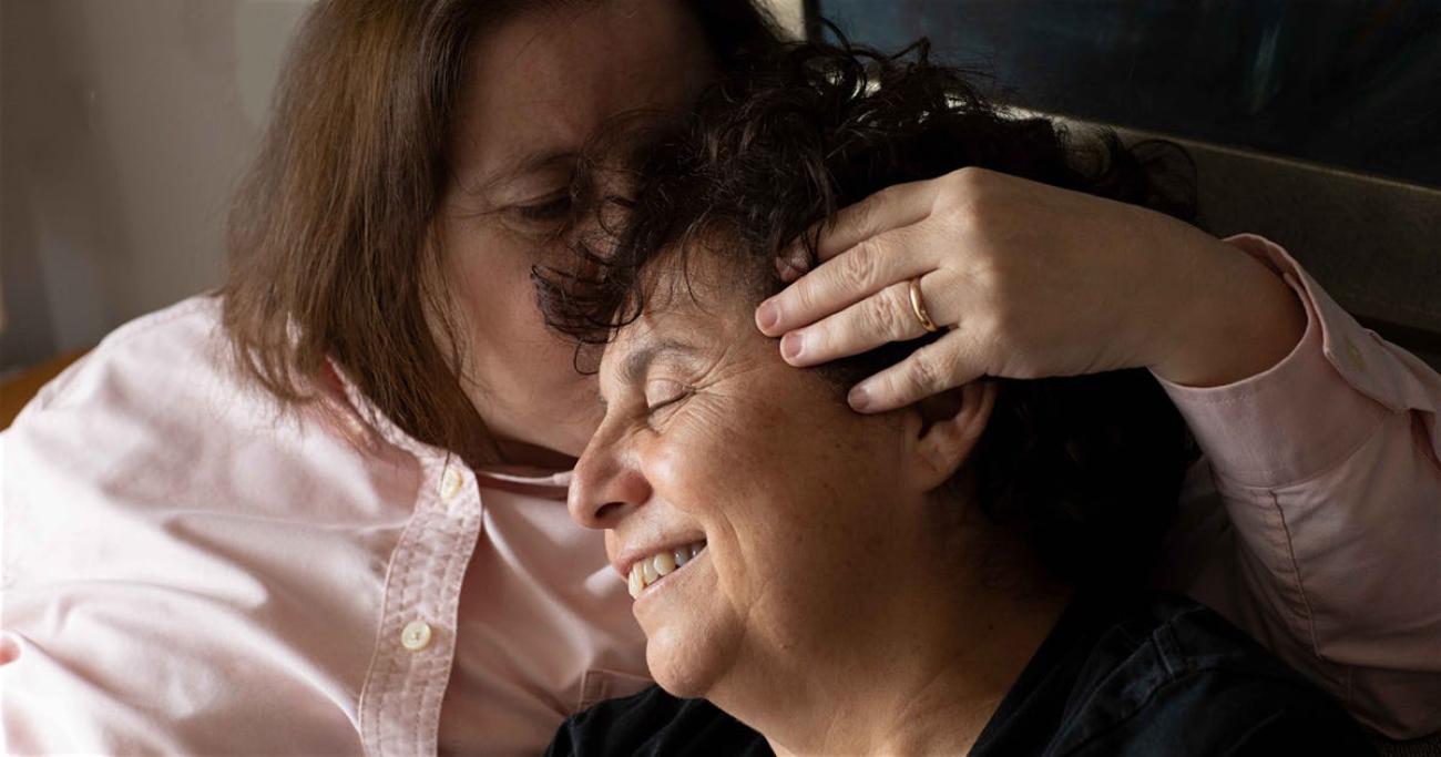 Deux femmes sourient tandis que l'une embrasse l'autre sur le front.