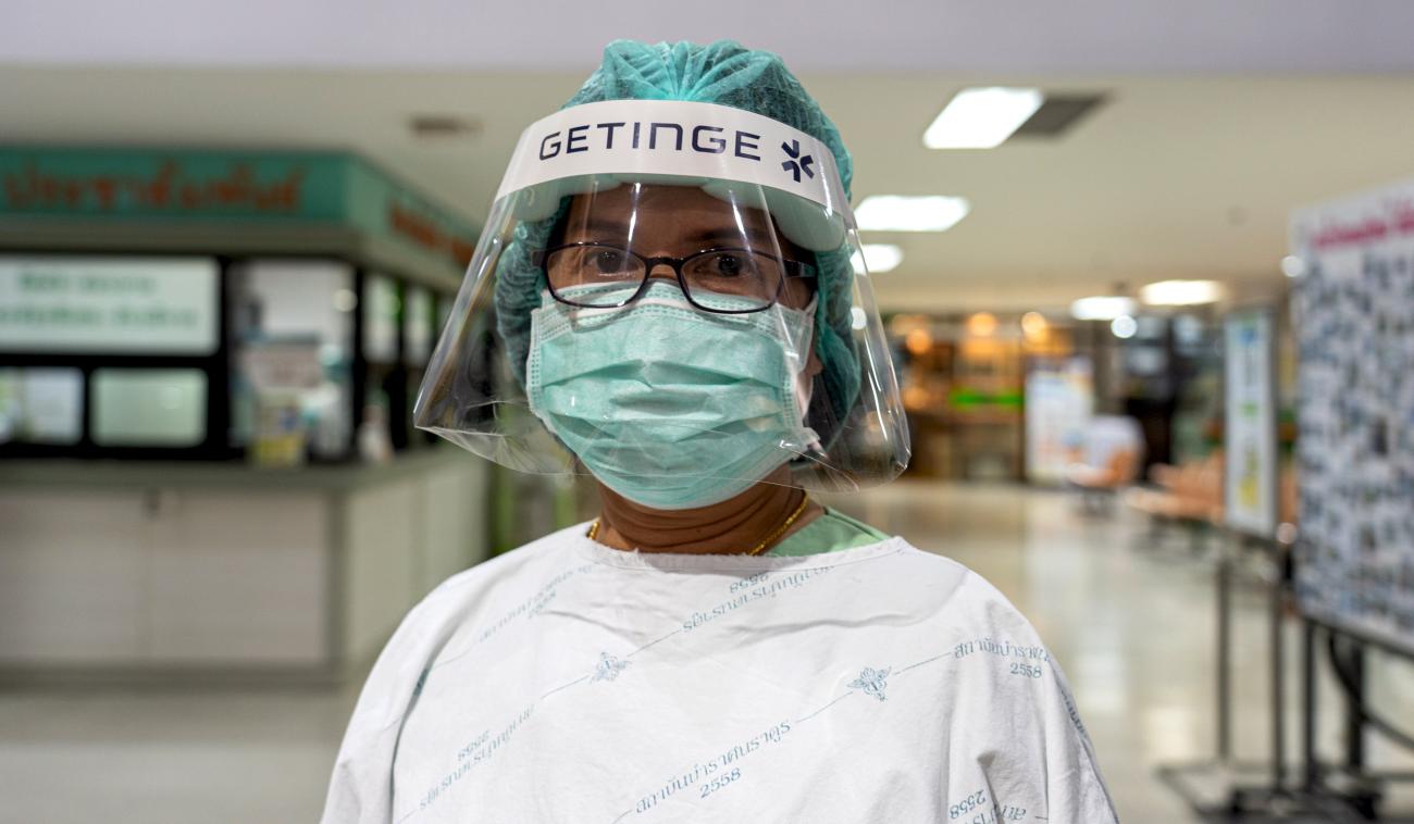 Une travailleuse de la santé se tient dans un hall de l'Institut des maladies infectieuses de Bamrasnaradura, en Thaïlande. Elle porte un équipement de protection individuelle ainsi qu’un masque chirurgical et une visière de protection.