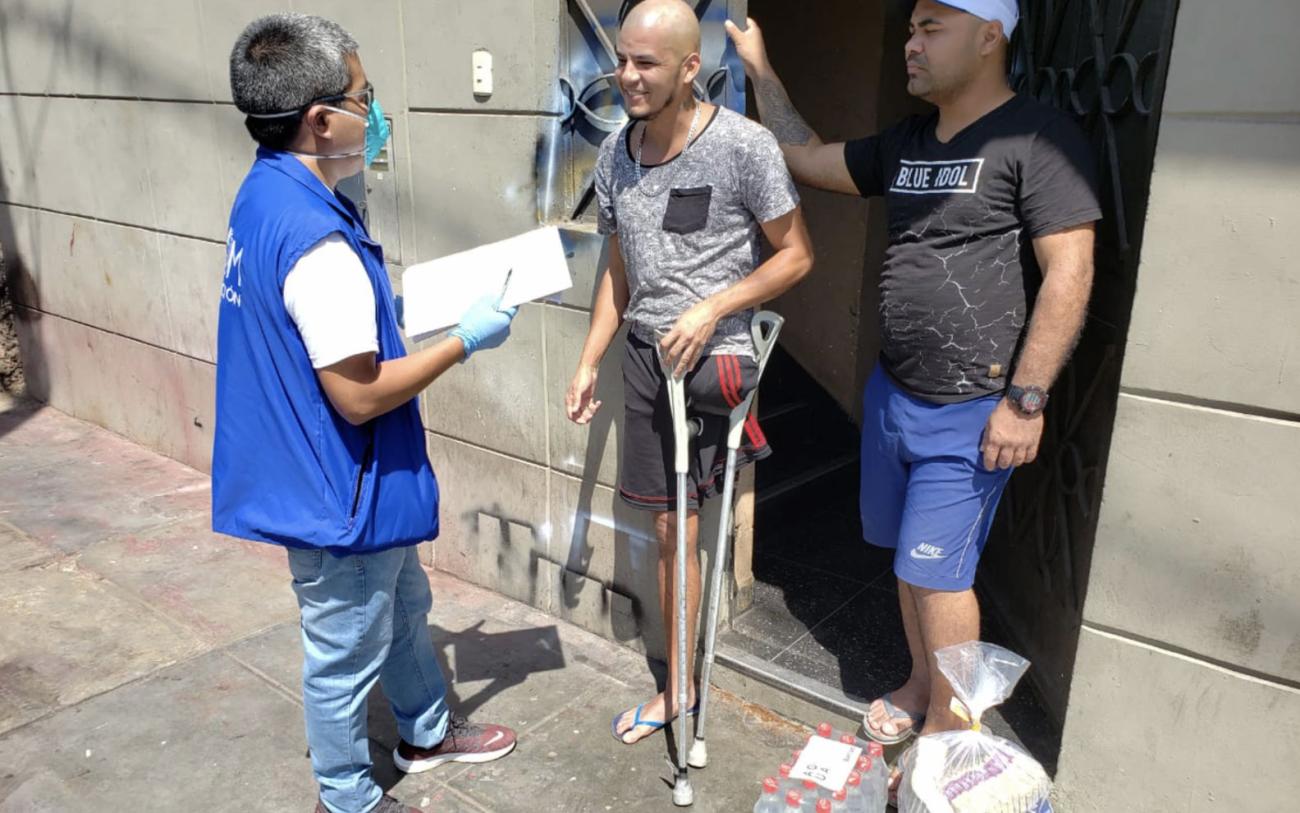 Un représentant de l'ONU se tient sur le seuil d’une porte devant deux hommes, dont l’un est amputé de la jambe gauche et s’appuie sur des béquilles. Le représentant de l'ONU s’entretient avec les deux hommes.