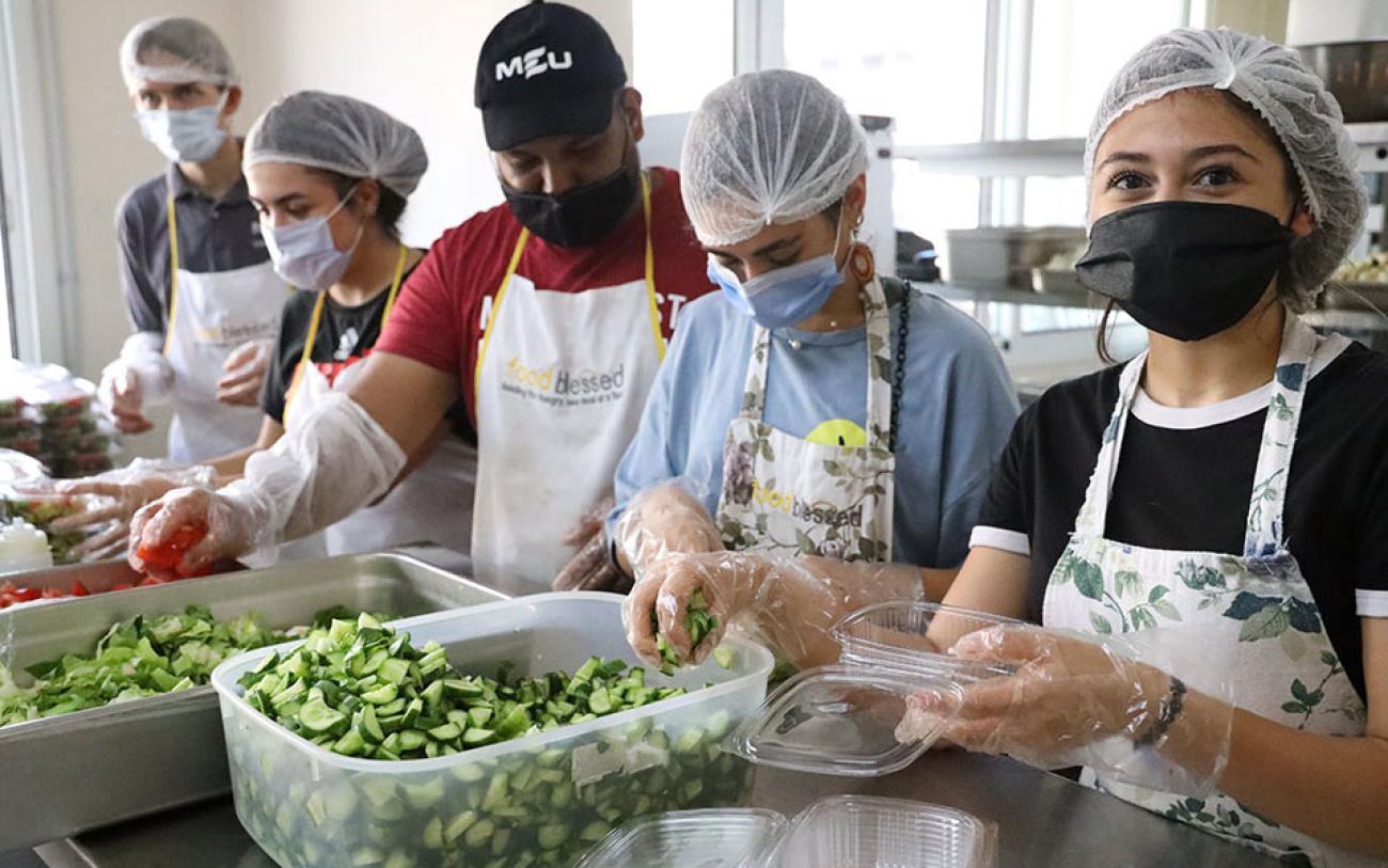 Hombres y mujeres jóvenes, usando mascarillas y redes para el cabello, preparan comidas en la cocina de Mairo en Sin El Fil, Beirut.