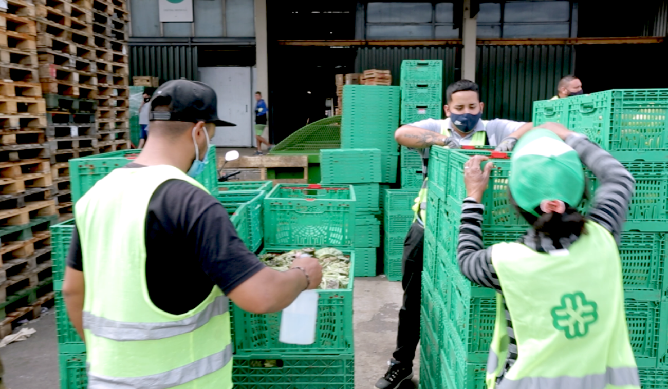 Los trabajadores del mercado central, considerados personal esencial, se apresuran a descargar cajas de mercancías durante la pandemia de COVID-19. Todos llevan mascarillas protectoras.