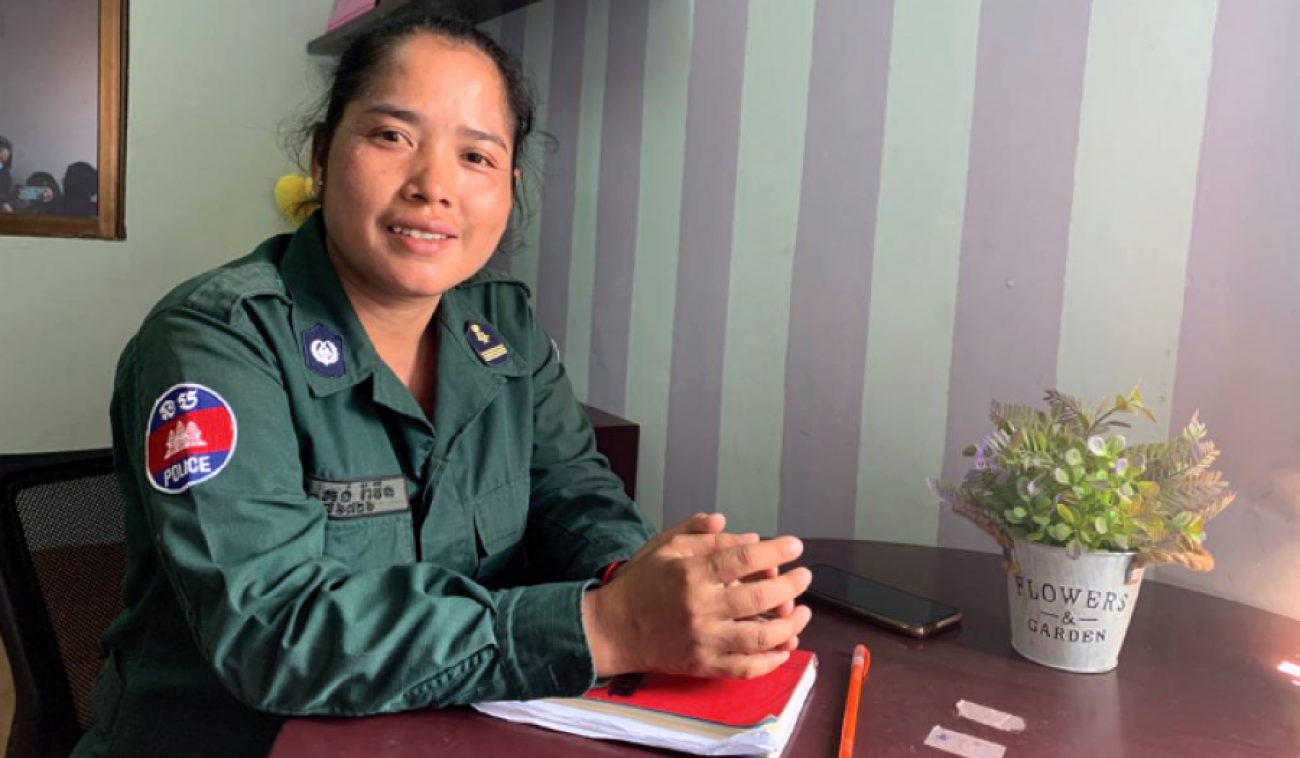 La agente de policía Kong Ravin, sonríe a la cámara mientras está sentada con su uniforme y las manos juntas sobre una mesa.