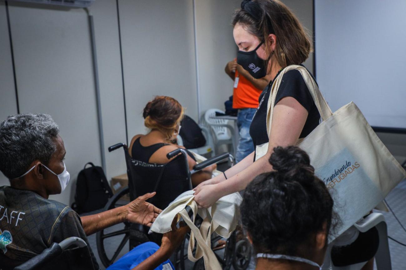 Plusieurs femmes, dont certaines en fauteuil roulant, sont réunies dans une salle pour recevoir une formation. Une femme membre du HCR portant un masque de protection tend à l’une des participantes un sac fourre-tout en tissu.