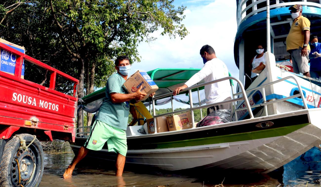 رجل يسير على الشاطئ بالقرب من قارب وهو يحمل المساعدات من موظفي المنظمة الدولية للهجرة.