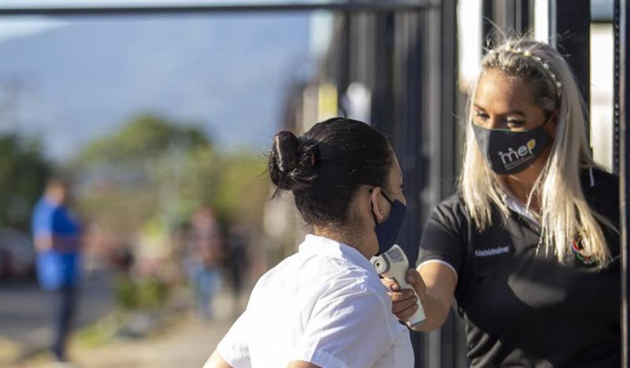 معلمة تفحص درجة حرارة الفتاة قبل دخول المدرسة عند البوابة.