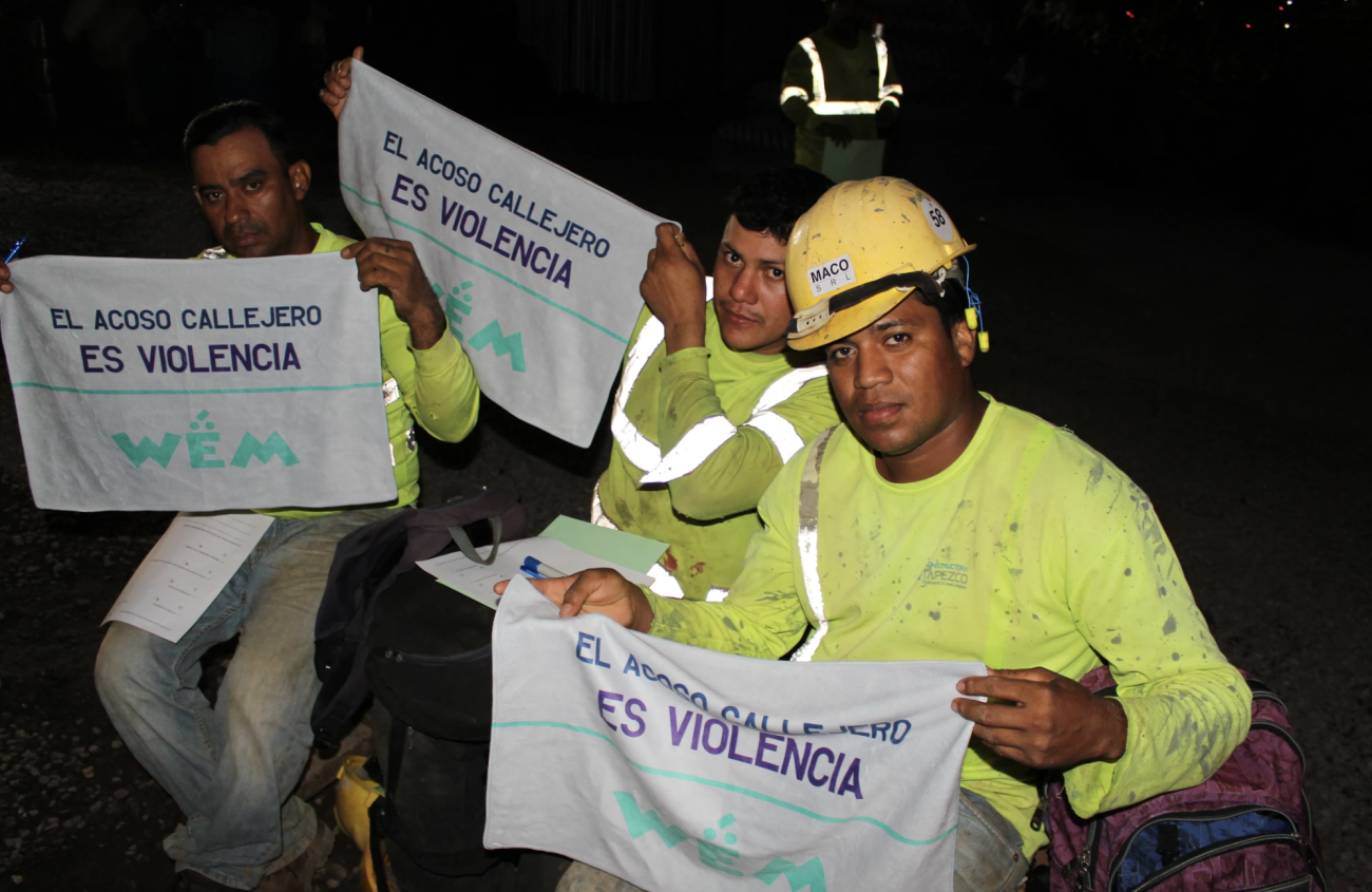 ثلاثة رجال يرتدون قمصانًا صفراء يحملون مناشف كتب عليها "تُعتبر المعاكسات في الشارع عنفًا ضد المرأة".