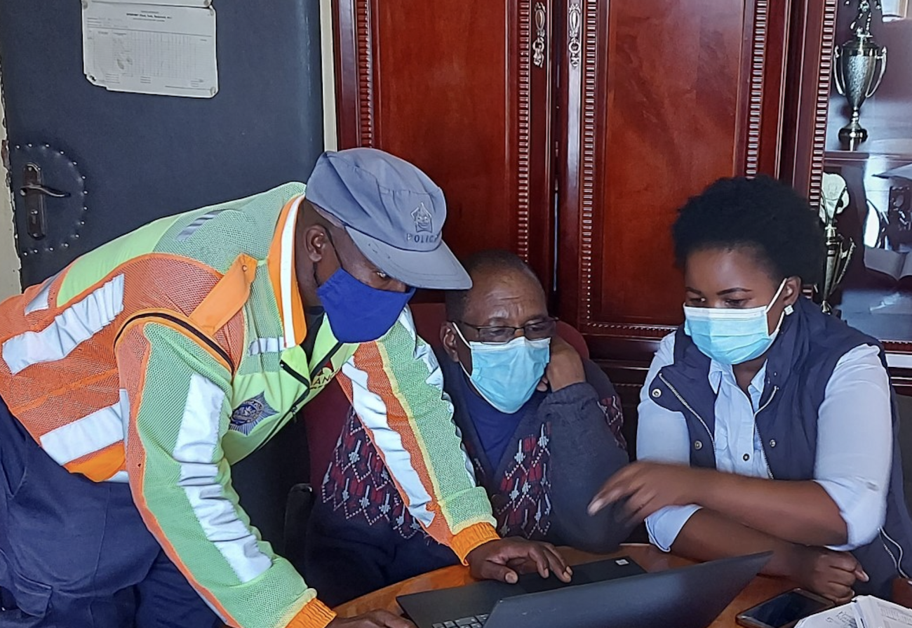 رجل يرتدي كمامة وقبعة يساعد شخصين لمساعدتهما على استخدام الكمبيوتر.