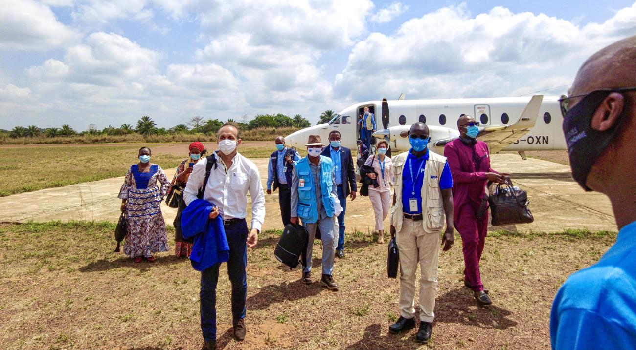 ينزل أشخاص عدة يرتدون أقنعة الوجه ويحملون أكياسًا وسترات إلى حقل في يوم مشمس.