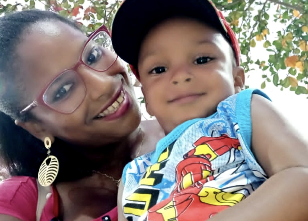 امرأة ترتدي قميصًا ظهريًا ونظارة تبتسم للكاميرا، وطفل يرتدي قميصًا من دون أكمام وقبعة حمراء.