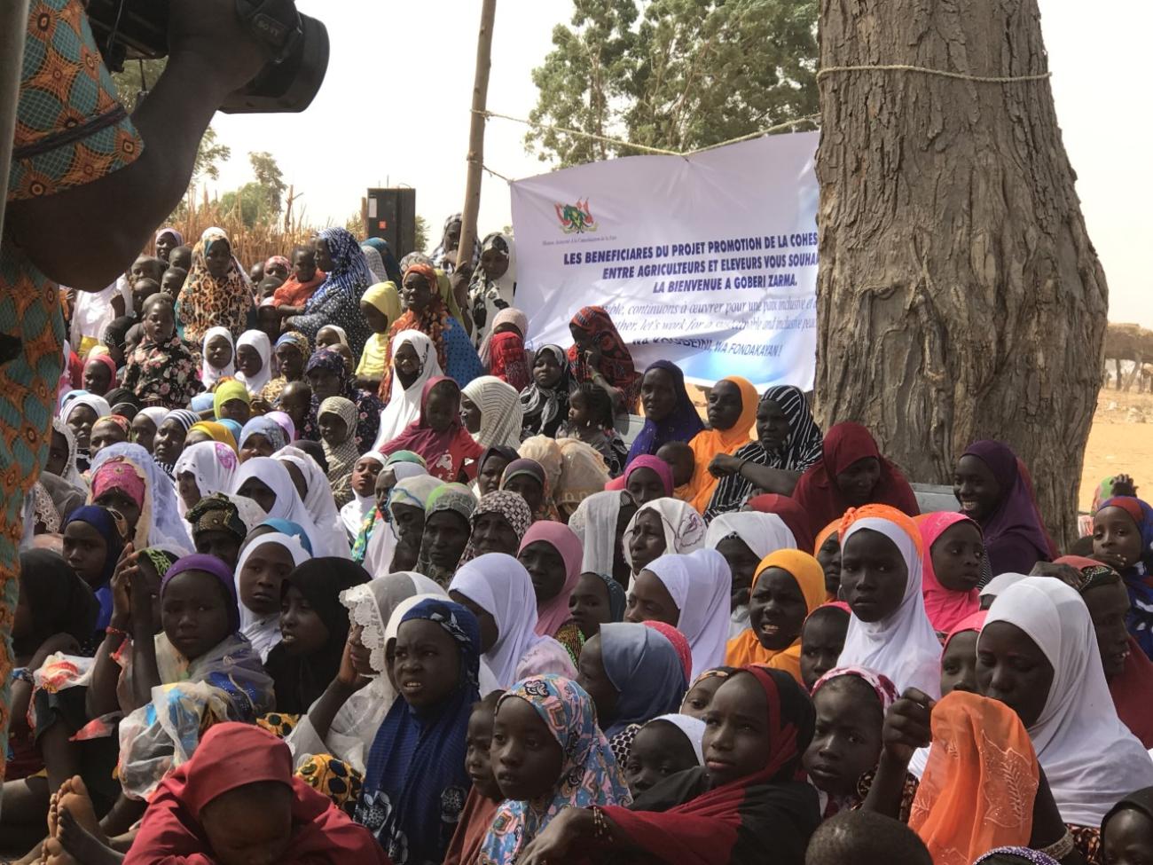 A large group of stand together in front of a large white banner with words in French.