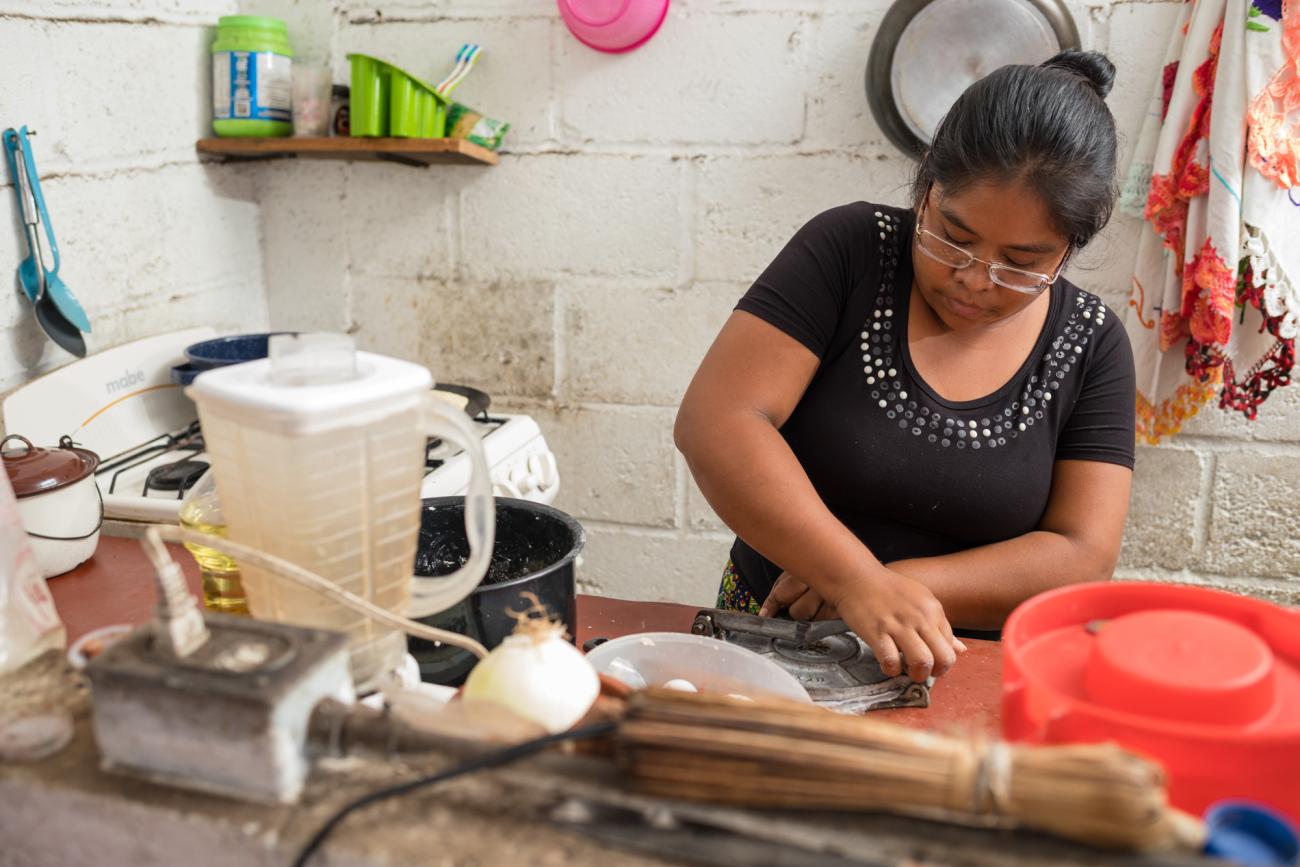 Une femme vêtue d'un haut noir prépare un repas dans une cuisine.