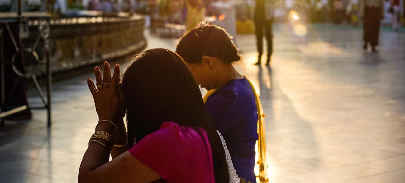 Two women praying outside while the sun is setting in the background. 