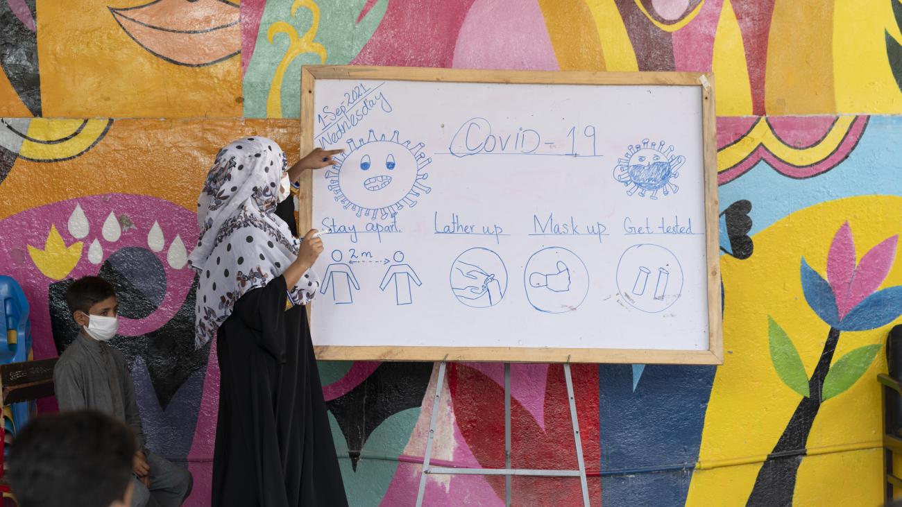 امرأة تشير إلى لوح أبيض كُتبت عليه معلومات عن بروتوكولات الأمان الخاصة بفيروس كوفيد-19.