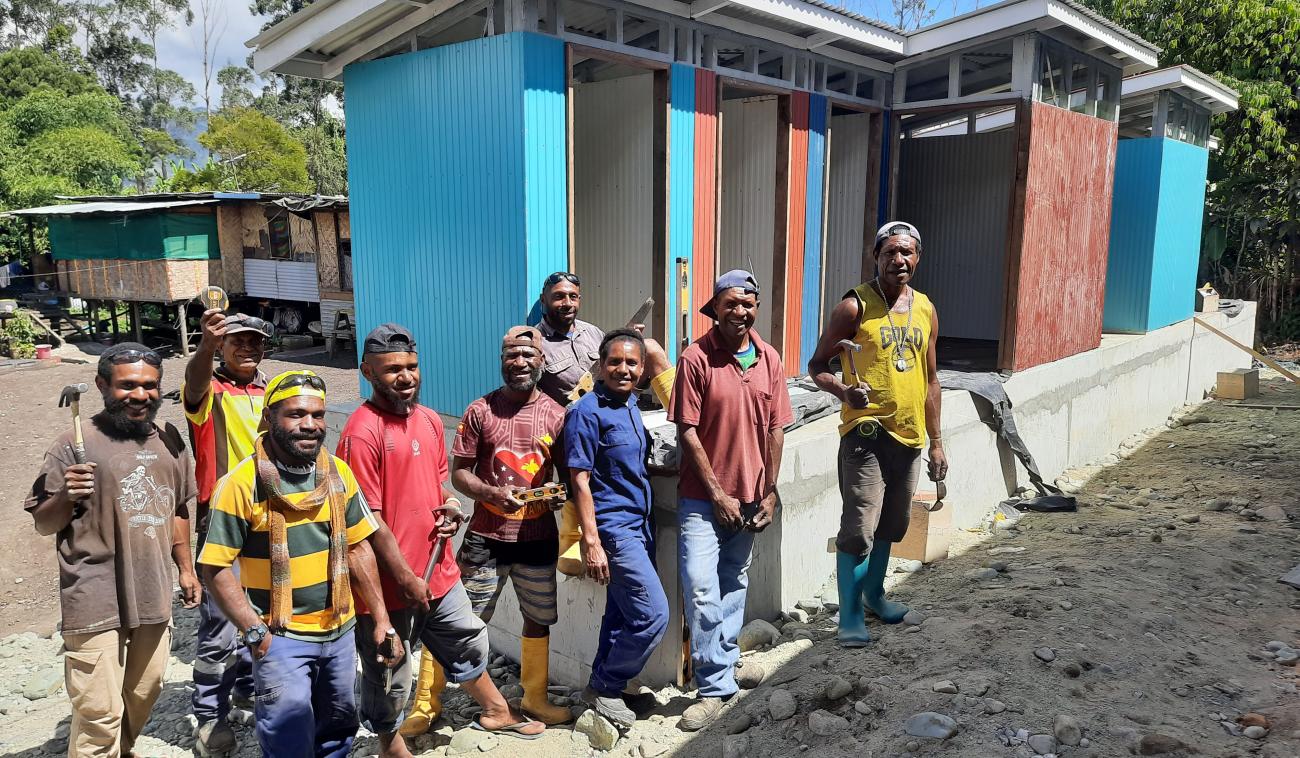 A group of men stand in front of multi-color latrines that they built. 