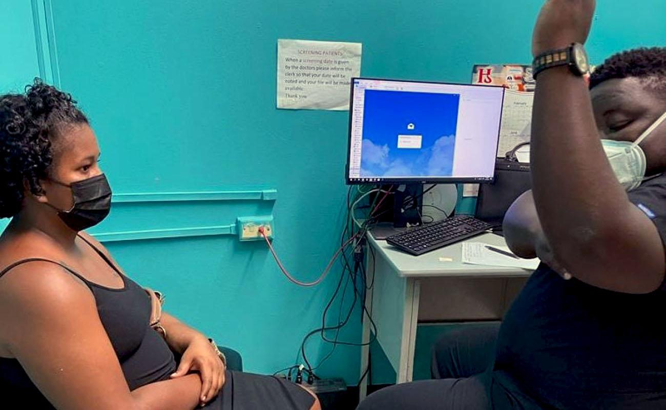 Un enfermero le muestra a una mujer sentada en una silla dónde se le colocará el implante en el brazo.