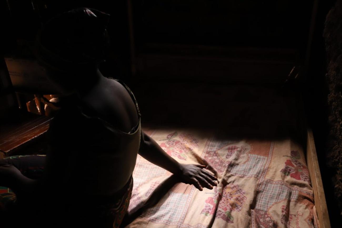 A silhouette of a girl sitting on a bed with one arm extended. 