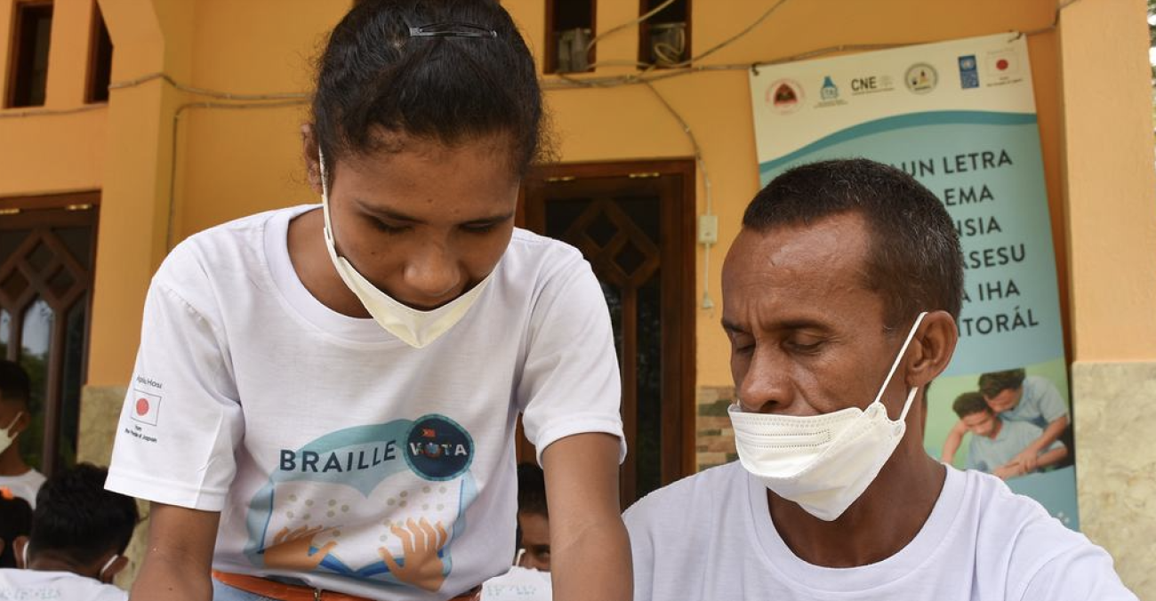 A woman in a white face mask leans over a man in a white face mask.