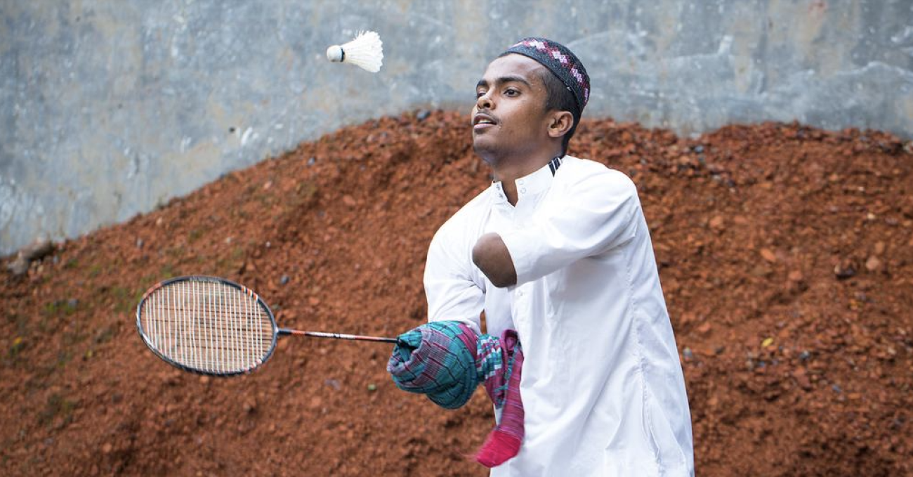 Un jeune homme  handicapé vêtu de blanc joue au badminton en plein air. 