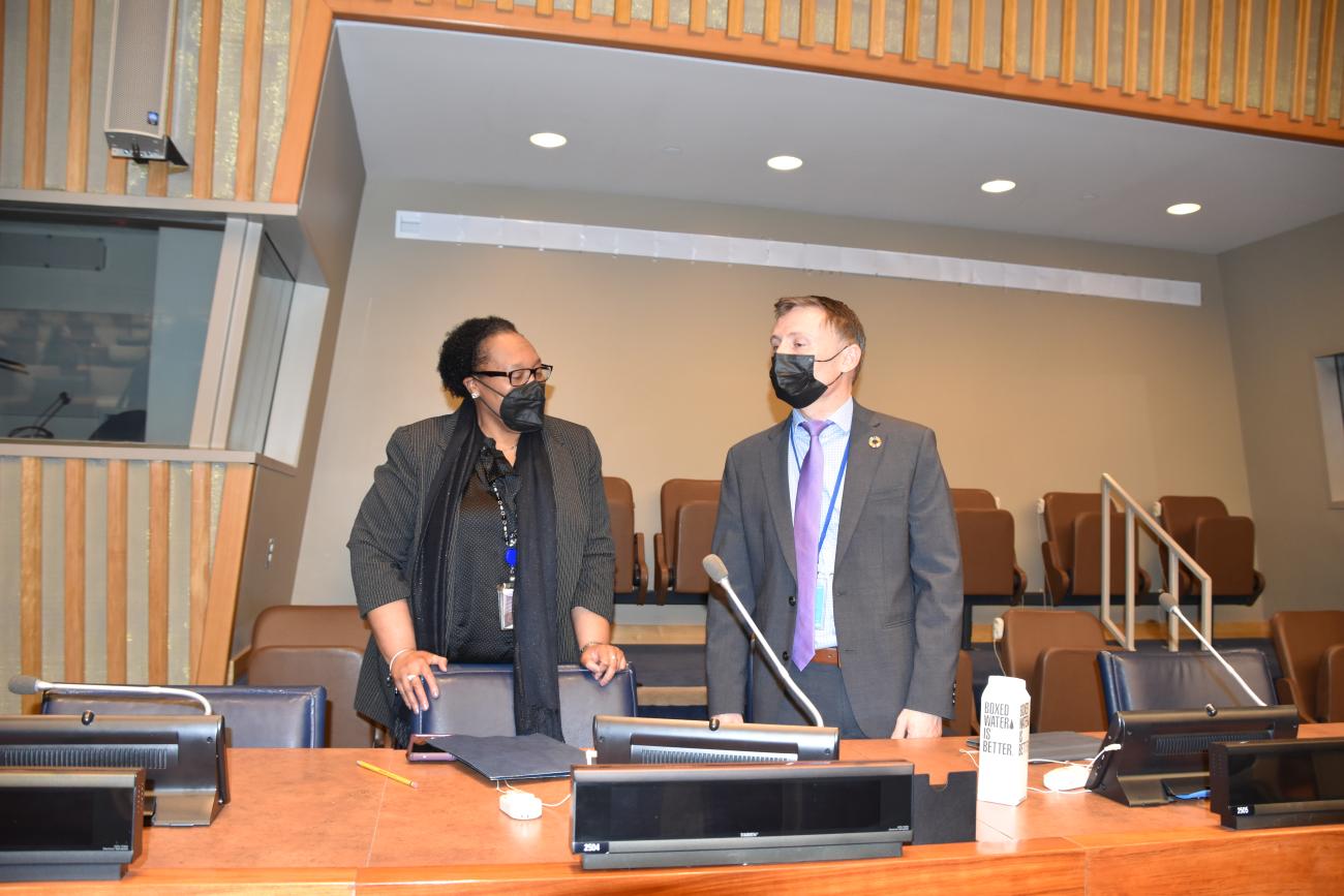 Una mujer y un hombre, ambos con mascarillas, hablan en una habitación acondicionada con madera.