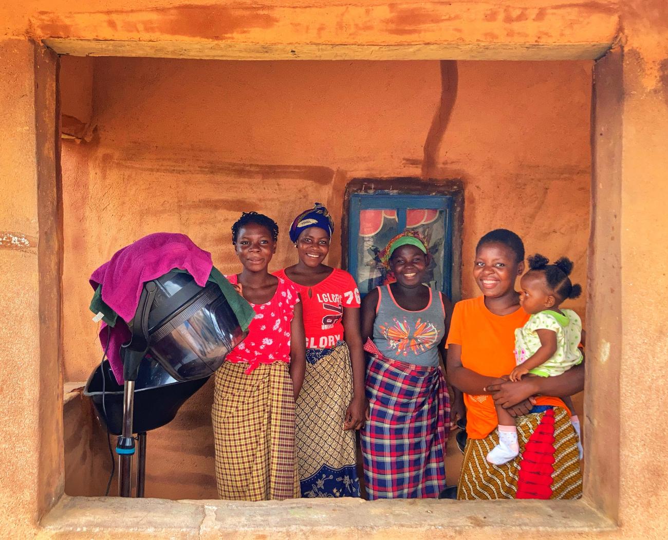 تقف نساء في غرفة مشمسة، وتحمل إحداهن طفلة.