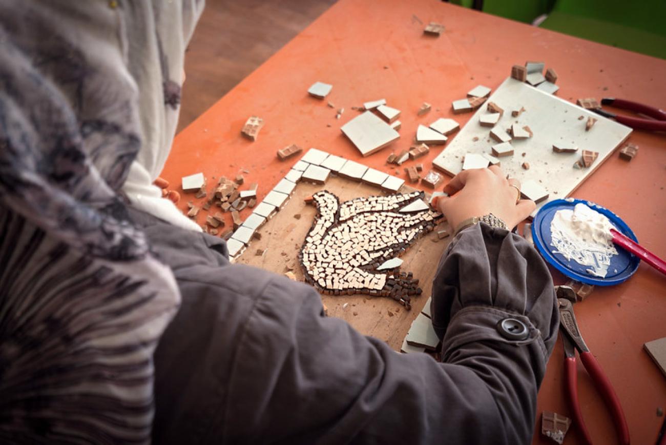 Une femme voilée est photographiée de dos en train de travailler avec des morceaux de mosaïque dans le cadre d'une atelier organisée par ONU Femmes.