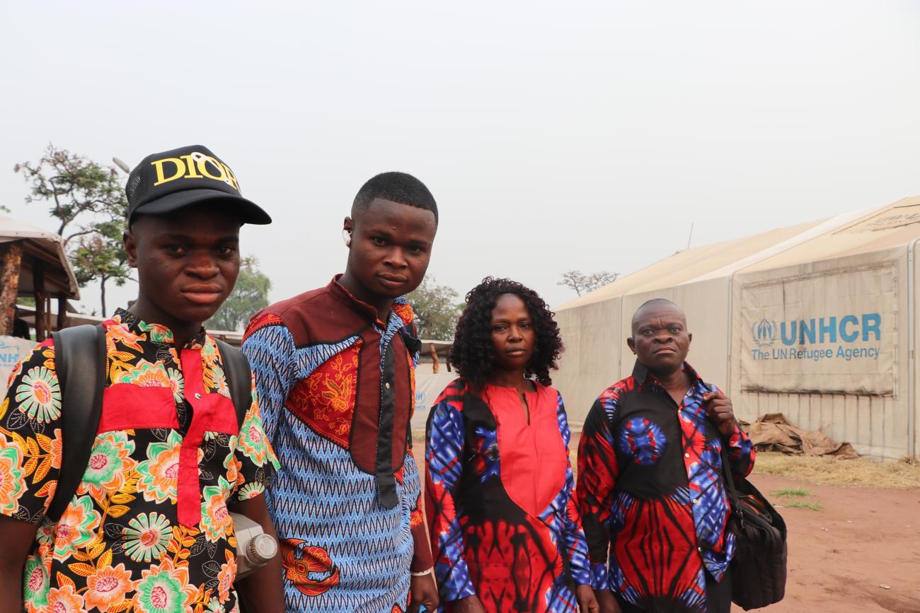 En Angola, deux jeunes hommes congolais se tiennent debout aux côtés de leur mère et de leur père devant un camp de réfugiés du HCR. Les quatre membres de la famille portent des vêtements bariolés et regardent en direction de l’objectif d’un air grave.